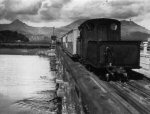 locomotive runs tender first across old river bridge