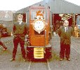 front view of red locomotive; one man in black suit on each side, wearing sunglasses